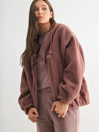 Model zipping up mauve sherpa jacket with side pockets and elastic cuffs.