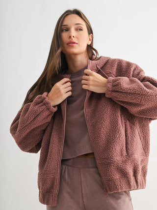 Woman wearing a mauve fleece zip-up hoodie with relaxed fit and drawstring hood.