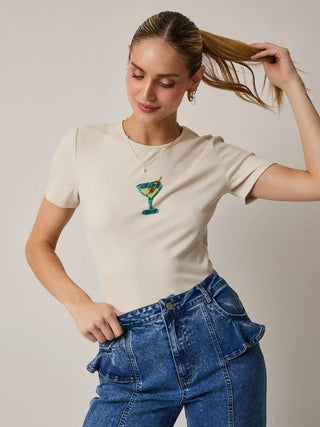 Model wearing a cream, ribbed, crop top with a beaded martini glass design, styled with high-rise denim.