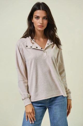 Woman wearing a light beige long-sleeve top with button details and blue jeans on a plain background