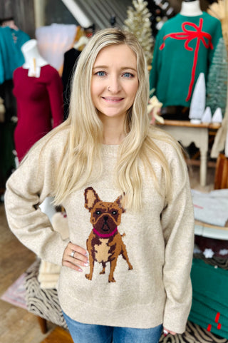 Woman wearing an oatmeal, knit, French Bulldog sweater inside boutique, showing full front view of the Frenchie graphic.
