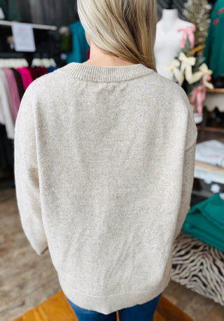 Back view of oatmeal, knit sweater showing relaxed fit and ribbed neckline.