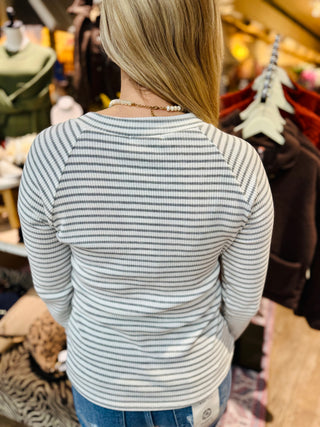 Back view of a woman wearing the ivory and grey striped knit long-sleeve top, showing the ribbed texture and fitted silhouette.