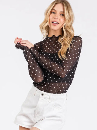 Model wearing black sheer polka dot blouse tucked into white shorts, front view
