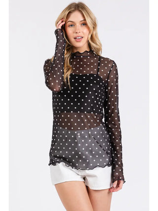Full-body front view of model wearing black and white polka dot sheer blouse with white shorts