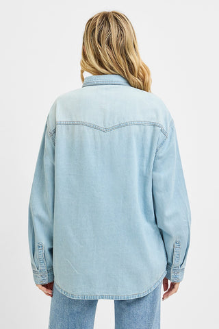 Back view of a relaxed fit western denim shirt featuring pointed yoke stitching across the shoulders and curved hemline.