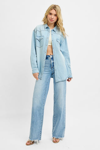 Full body view of a relaxed light wash denim shirt with western yoke detail, styled with wide leg denim jeans and a cropped top for a layered denim-on-denim look.