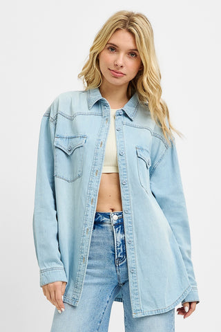 Model wearing a relaxed fit western-style denim button-up shirt with light wash, front chest pockets, and pointed yoke detail — styled open over a cropped tank.