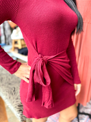Close-up of the waist tie detail on the burgundy ribbed knit dress showing the ribbed texture and gatherred side draping.