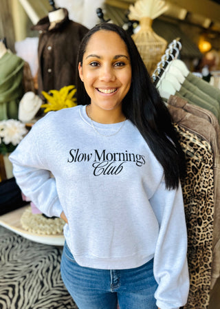 Woman wearing a 'Slow Mornings Club' sweatshirt in a store setting.
