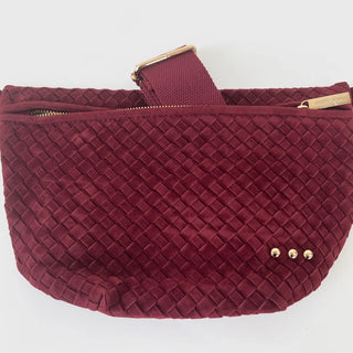 Flat lay of the burgundy Westlyn Suede Woven Bum Bag with strap and gold accents visible