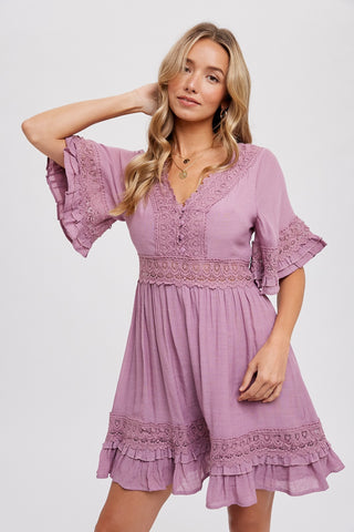 Model wearing a mauve rose mini dress with V-neckline, lace trim details, and flutter sleeves — features a smocked waistband and ruffle hemline for a flirty, feminine look.
