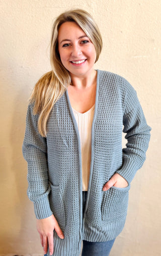 Model wearing the blue grey waffle knit cardigan with pockets styled over a neutral ribbed tank and denim
