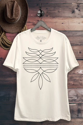 White unisex graphic t-shirt hanging on a wooden backdrop, featuring a bold black western boot stitch-inspired design printed on the front — styled with rustic elements like a cowboy hat and rope.