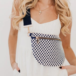 Close-up of a navy and white checkered bum bag with a solid navy strap and gold zipper detail, styled over a white dress.