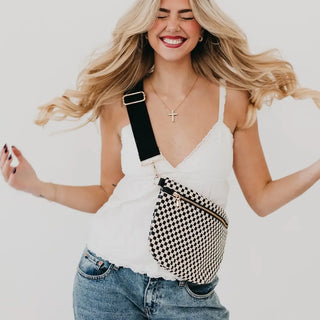 Model wearing the black and white checkered Westlyn bum bag with a wide black strap, styled crossbody over a white cami and denim.