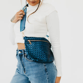 Model wearing the metallic navy blue Westlyn woven bum bag with matching navy and royal striped strap — styled crossbody over denim.