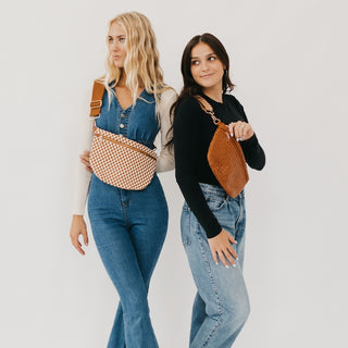 Two models wearing the Westlyn woven bum bag — one in the light mocha and white checkered pattern, and the other in solid light mocha. Each bag features a textured woven finish and thick adjustable strap worn crossbody.