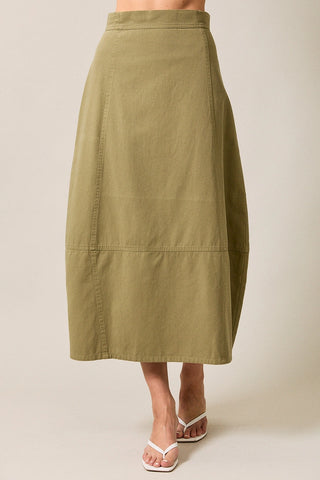 An olive green midi skirt with a tiered design and side seam detailing including a barrel shape, shown on a model wearing white thong sandals against a light beige background.