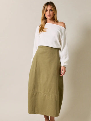 A woman modeling a white off-the-shoulder long-sleeve top and an olive green midi skirt with a barrel style shape against a plain beige studio background.