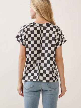 View of a woman shown from the back wearing a black and white checkered short-sleeve knit top with raw edge details around the sleeve hem, collar, and down the middle of the back and light blue jeans against a plain light background.