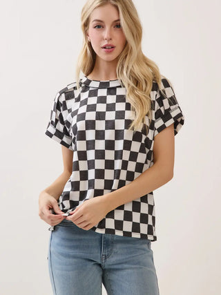 A woman modeling a black and white checkered short-sleeve knit t-shirt with light blue jeans, standing against a plain off-white background.