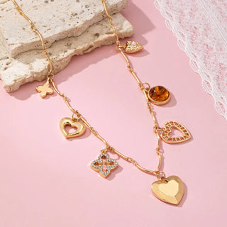 Close-up of sweet charm collection featuring lucky clover, pearl heart, amber gem and lattice heart on gold necklace