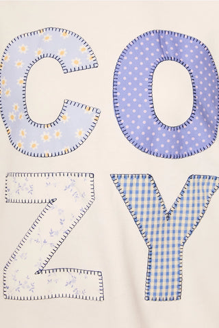 Close-up of COZY patchwork applique on cream sweatshirt with floral, polka dot, and gingham letters outlined in stitching.
