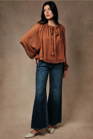 Full-length front view of rust crinkle chiffon peasant blouse styled with wide-leg jeans and mule heels