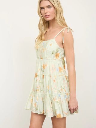 Side view of woman wearing a light sage green floral dress showing the spaghetti strap ties and mini length.