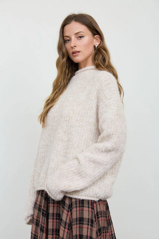 Side view of women's oversized cream fuzzy knit mock neck sweater with long drop shoulder sleeves and raw edge trim detail