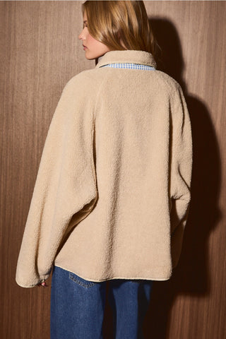 Back view of beige reversible sherpa jacket showing relaxed oversized fit and blue gingham detail beneath the collar.