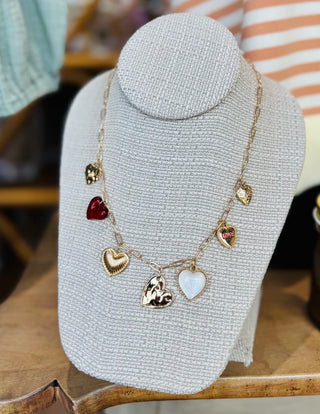 Close-up of seven different heart charm designs including open hearts, puffed hearts and pearl hearts on gold necklace