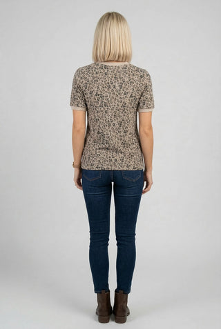 A woman viewed from behind wearing a short-sleeve crewneck, short sleeve, leopard top with a beige and brown leopard print, paired with dark blue skinny jeans and brown ankle boots, against a light gray studio background.
