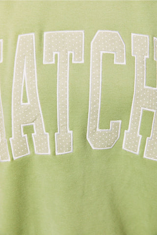 Close-up of Matcha embroidery on green sweatshirt – off-white polka dot letter applique with white border detail on light matcha green fabric