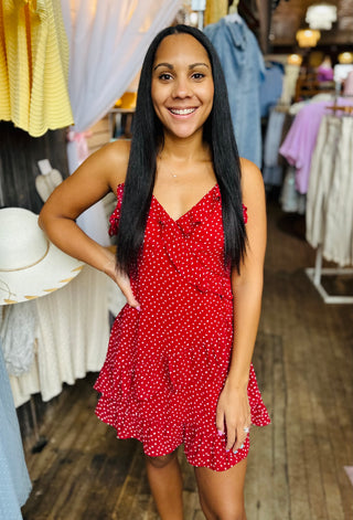Woman wearing a red polka dot mini dress  with spaghetti straps and an asymmetrical hem