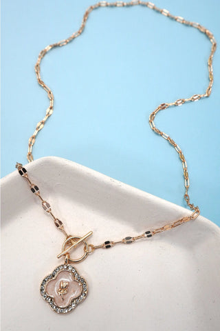 Rhinestone rose flower charm toggle necklace with gold paperclip chain displayed on white ceramic tray against blue background