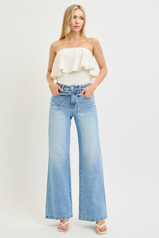 Model wearing Risen high rise wide leg jeans with tie waist detail paired with white ruffled tube top – full length front view in light wash