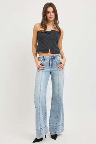 Model wearing Risen tummy control mid rise ankle wide flare jeans in light wash paired with black strapless crop top – full length front view showing pintuck leg detail