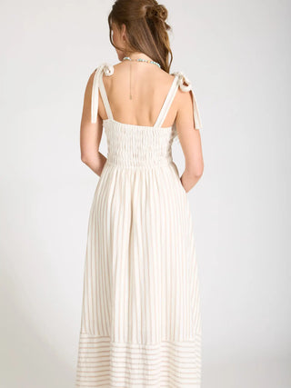 Back view of woman wearing a smocked bodice, midi length striped dress showing open upper back with tied straps.