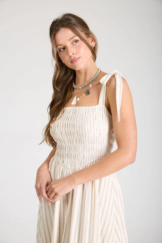 Close up view of woman wearing a striped dress showing basque waist with smocked bodice and square neckline and tied shoulder straps.