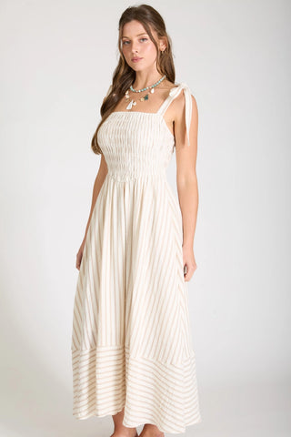 Side view of woman wearing a striped, basque waist, midi length dress. Showing flared skirt portion and bow tied straps.